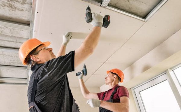 Installation of drywall. Workers are using screws and a screwdriver to attach plasterboard to the ceiling.